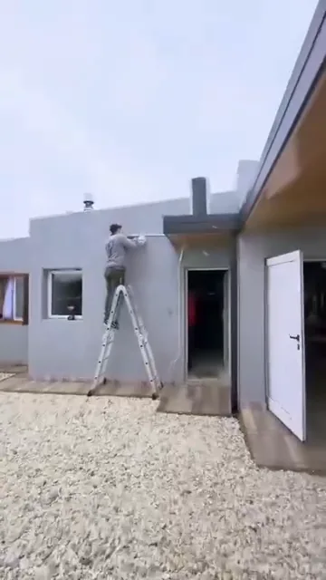 Instalador trabajando sobre una escalera en el exterior de una vivienda moderna, durante la etapa de terminaciones