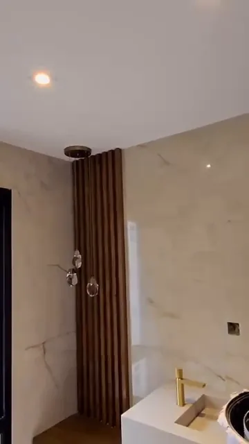 Bachas suspendidas sobre mármol con aplique de pared en madera y luces colgantes encendidas
