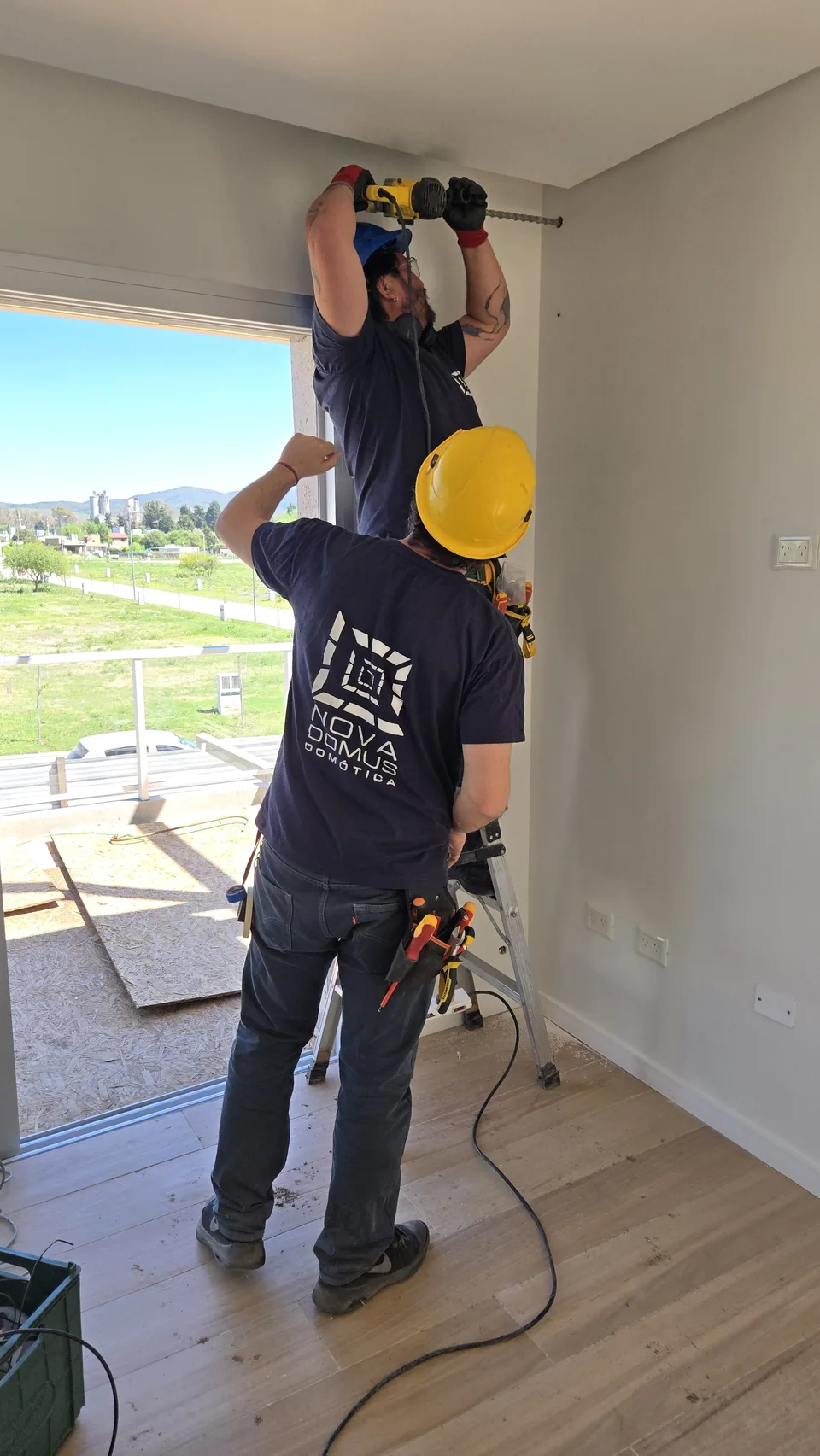 Dos técnicos de Nova Domus trabajando en el cielorraso de un ambiente en obra, con vista al paisaje serrano